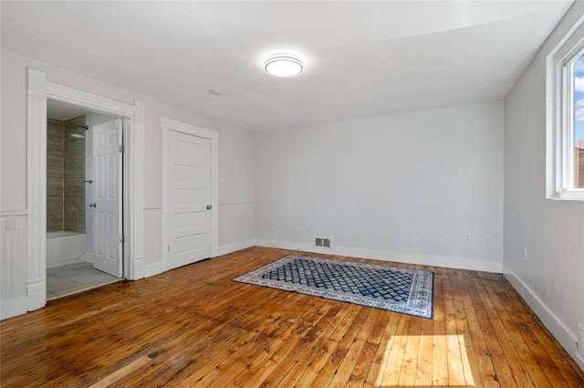 unfurnished bedroom with ensuite bath, hardwood / wood-style flooring, baseboards, and visible vents