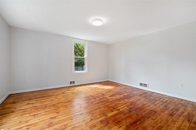 spare room featuring baseboards, wood-type flooring, and visible vents