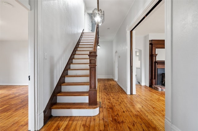 stairway featuring a fireplace, baseboards, hardwood / wood-style floors, and a notable chandelier