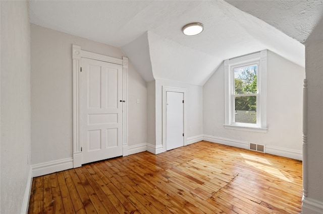 additional living space featuring visible vents, baseboards, lofted ceiling, and hardwood / wood-style floors