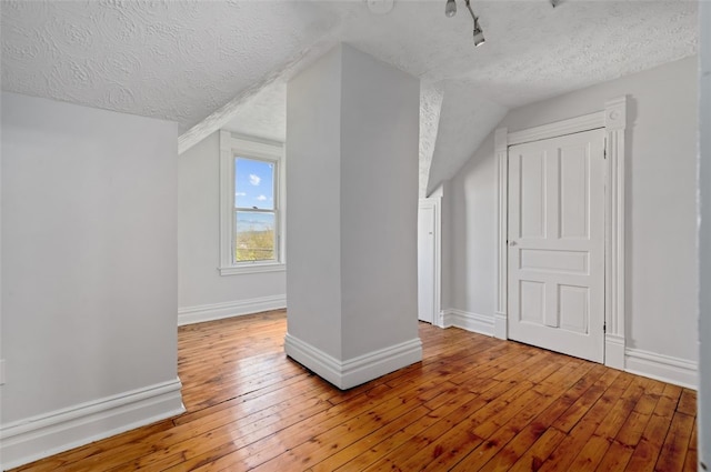 additional living space with a textured ceiling, vaulted ceiling, baseboards, and hardwood / wood-style flooring