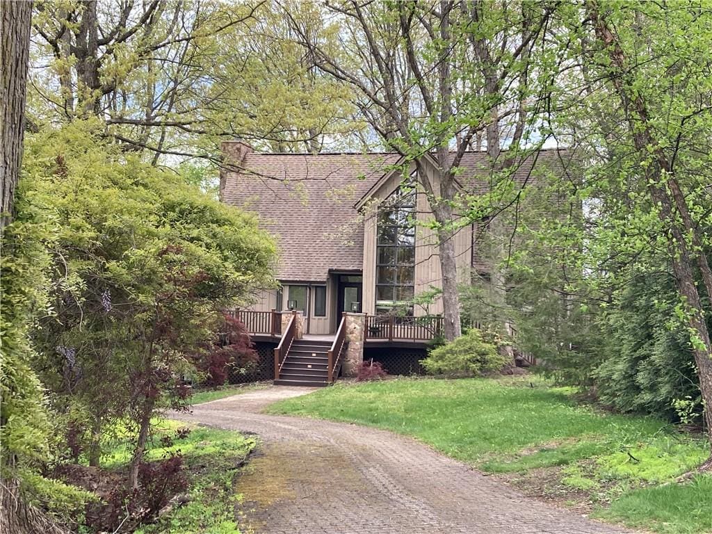 view of front of house featuring a chimney, a deck, a front lawn, and a shingled roof