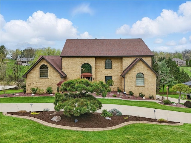 view of front of property with brick siding, roof with shingles, and a front yard