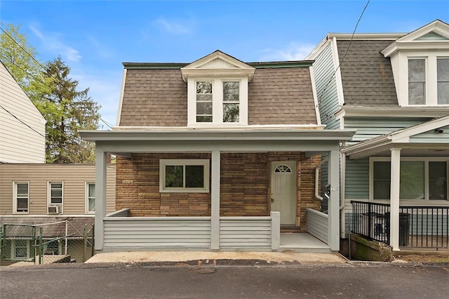 view of front facade with a porch, roof with shingles, fence, and mansard roof
