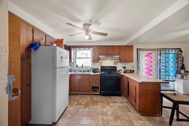 kitchen featuring black range with gas cooktop, freestanding refrigerator, under cabinet range hood, a sink, and a peninsula