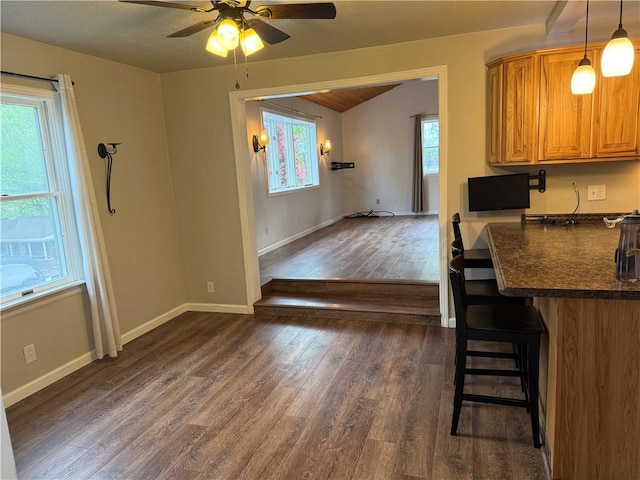 kitchen with a kitchen bar, dark countertops, dark wood finished floors, baseboards, and ceiling fan
