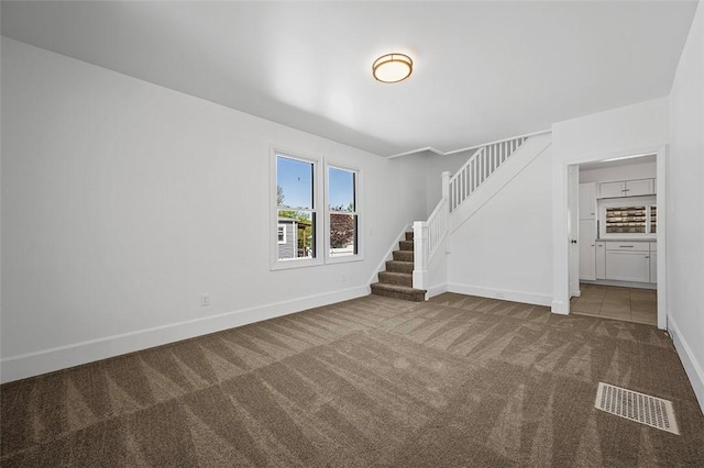 unfurnished living room featuring carpet, visible vents, baseboards, and stairway