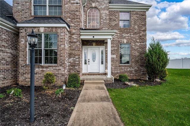 view of exterior entry with brick siding, fence, and a lawn