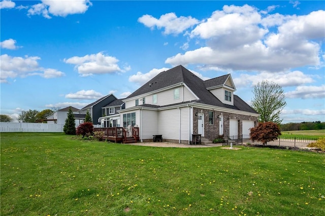 rear view of property with fence, an attached garage, a deck, brick siding, and a lawn