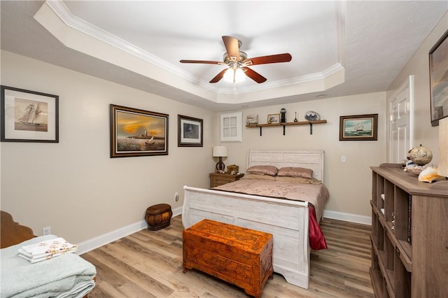 bedroom with a tray ceiling, wood finished floors, baseboards, and ornamental molding