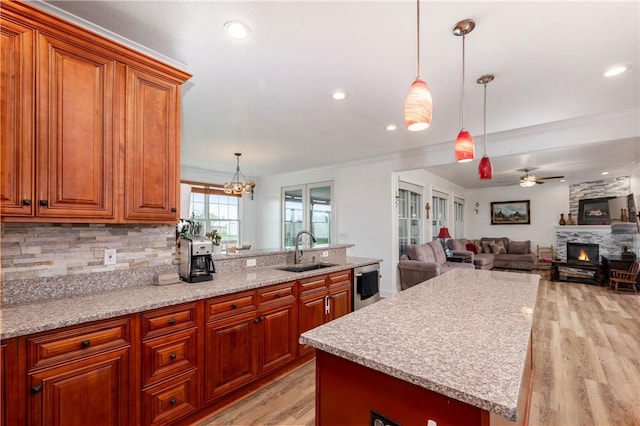 kitchen with dishwasher, brown cabinetry, a sink, a fireplace, and light wood-type flooring