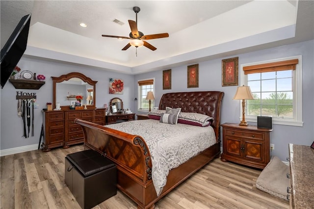 bedroom with a tray ceiling, baseboards, light wood finished floors, ceiling fan, and visible vents
