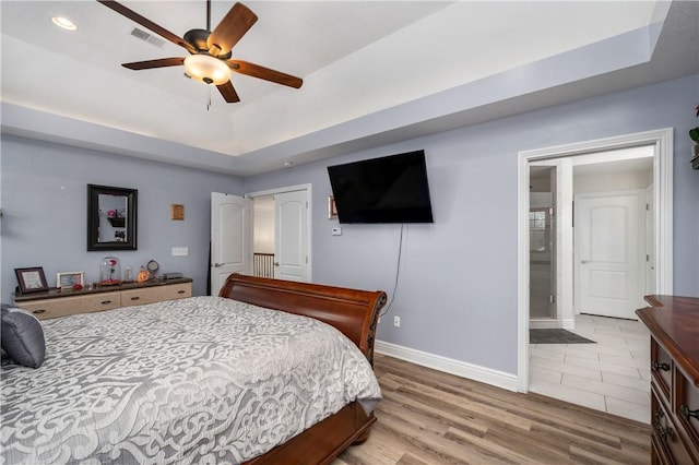 bedroom featuring recessed lighting, baseboards, connected bathroom, a raised ceiling, and light wood-style floors