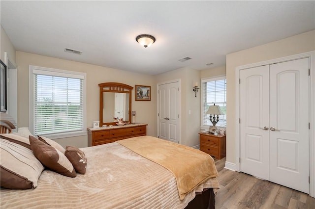 bedroom featuring light wood finished floors, two closets, visible vents, and baseboards
