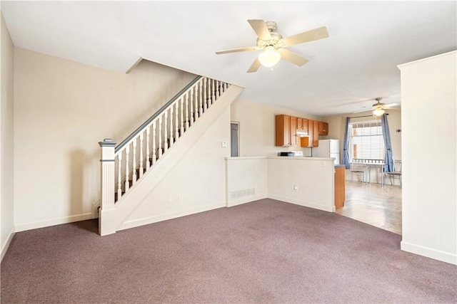 unfurnished living room with a ceiling fan, visible vents, baseboards, stairway, and dark colored carpet