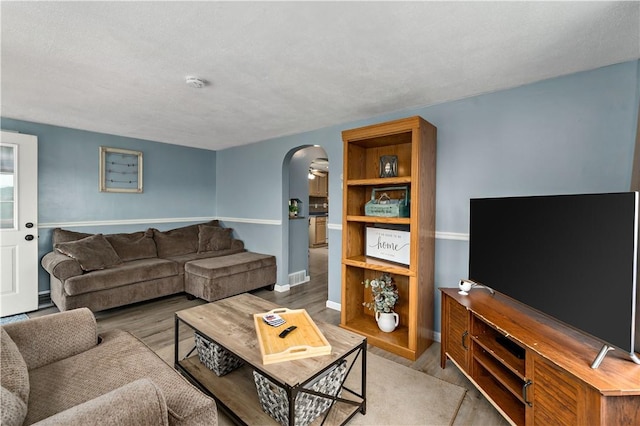 living area with arched walkways, baseboards, visible vents, and wood finished floors