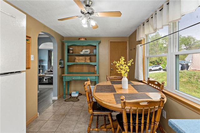 dining room with ceiling fan, arched walkways, baseboards, and light tile patterned floors