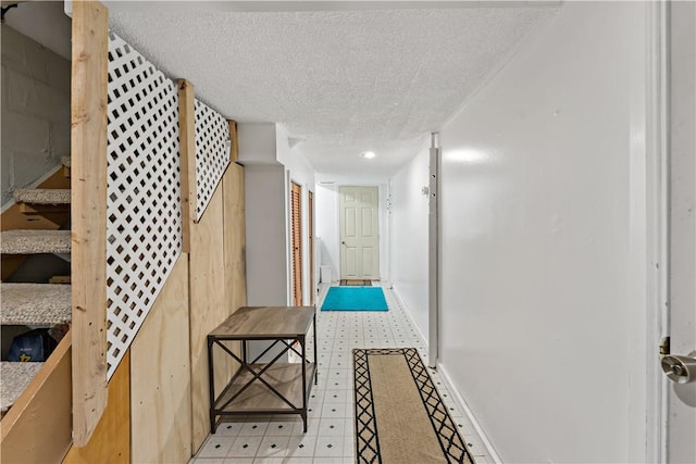 hall featuring light floors, a textured ceiling, stairs, and baseboards
