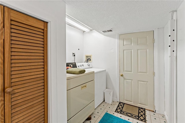 laundry room with washing machine and clothes dryer, light floors, visible vents, and a textured ceiling