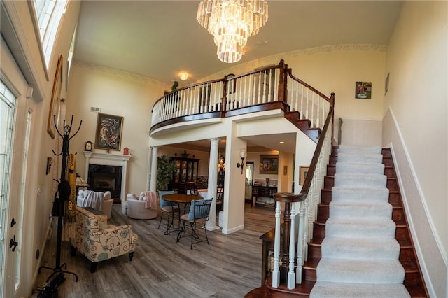 stairway featuring a high ceiling, wood finished floors, a chandelier, a fireplace, and baseboards