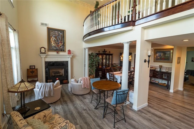 living area with ornate columns, wood finished floors, a towering ceiling, a premium fireplace, and baseboards