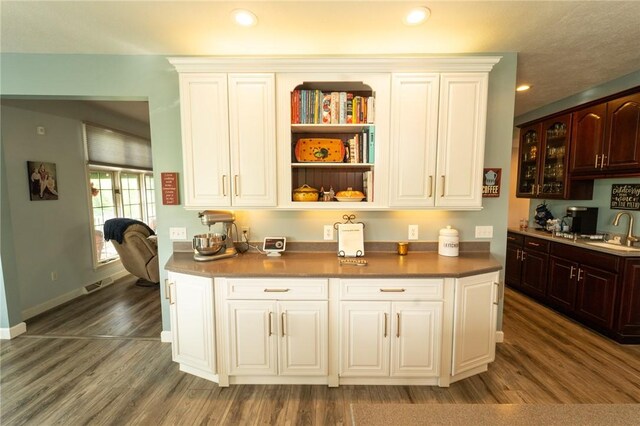 kitchen with a sink, wood finished floors, glass insert cabinets, dark brown cabinetry, and recessed lighting