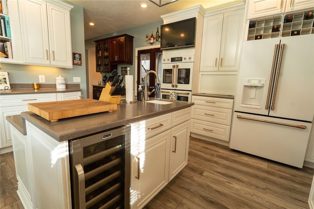 kitchen featuring white appliances, beverage cooler, dark countertops, a sink, and dark wood-style flooring