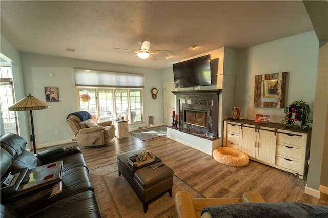 living room with wood finished floors, ceiling fan, baseboards, and a high end fireplace