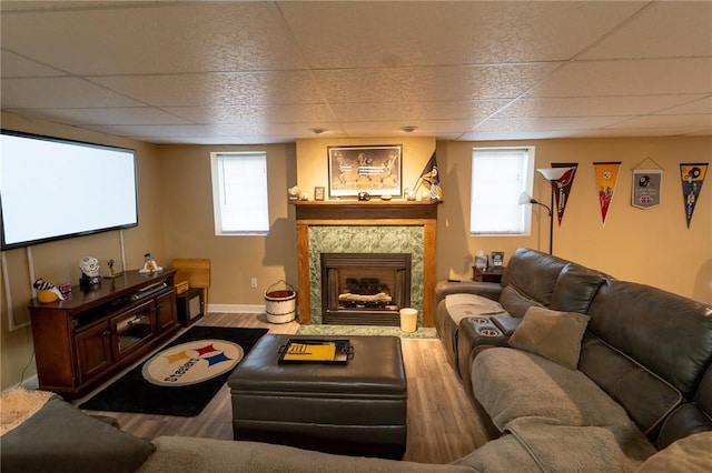 living area featuring a paneled ceiling, wood finished floors, baseboards, and a tile fireplace