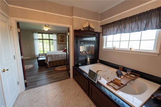ensuite bathroom featuring a tub with jets, a sink, and a ceiling fan