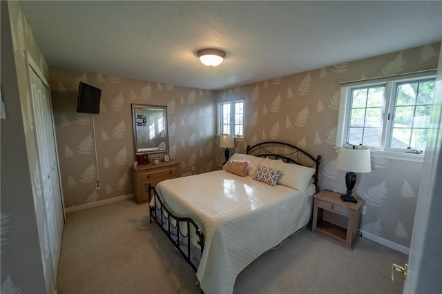 bedroom featuring wallpapered walls, light carpet, baseboards, and a closet