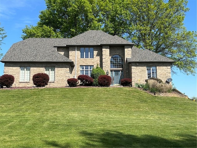 view of front of house featuring a front lawn, a shingled roof, and brick siding