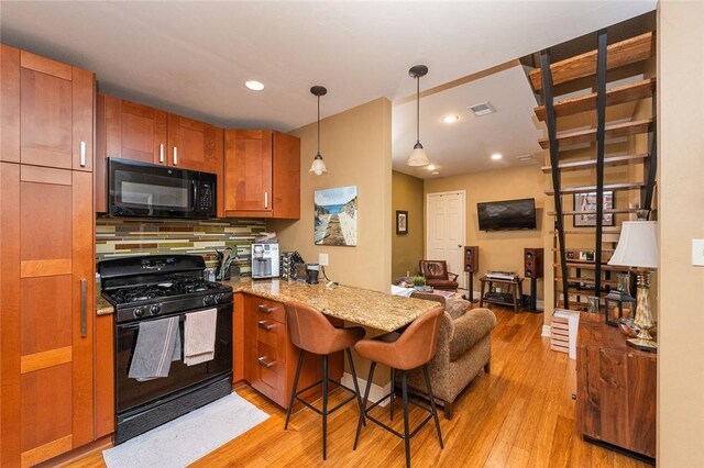 2220 Sarah St, South Side, PA 15203 - kitchen featuring black appliances, a peninsula, light wood-type flooring, decorative light fixtures, and light stone counters