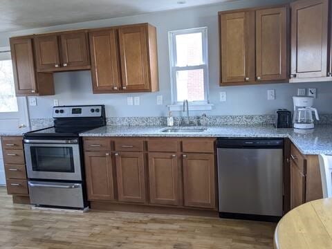 kitchen featuring appliances with stainless steel finishes, a sink, light wood-style floors, brown cabinets, and light stone countertops