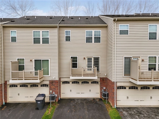 back of house with an attached garage, brick siding, asphalt driveway, and central AC unit