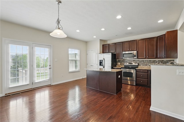 kitchen with appliances with stainless steel finishes, a center island, dark brown cabinets, dark wood-style floors, and backsplash