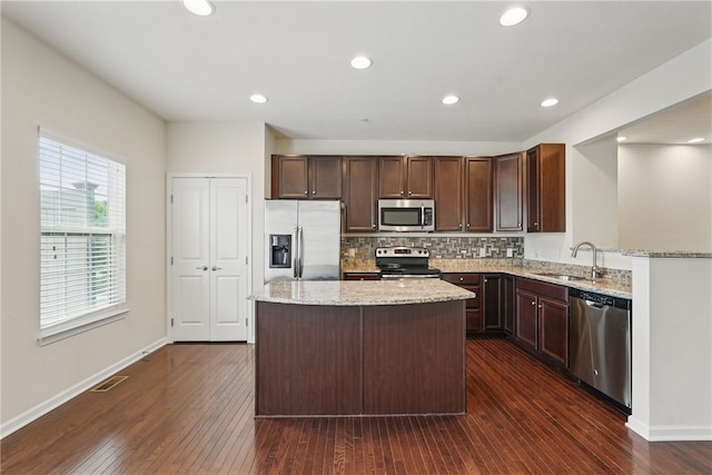 kitchen featuring stainless steel appliances, a sink, dark wood-type flooring, light stone counters, and recessed lighting