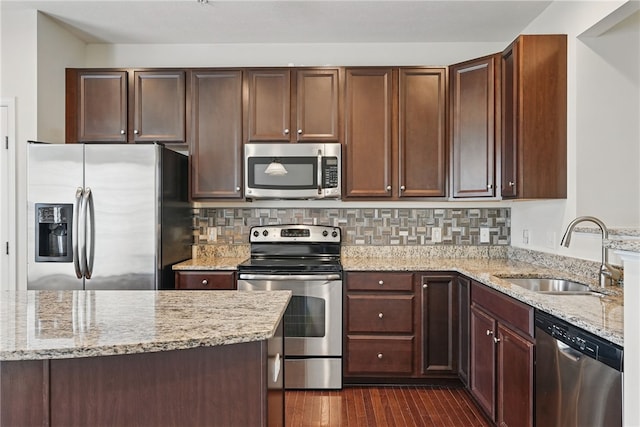 kitchen featuring appliances with stainless steel finishes, a sink, light stone counters, dark wood finished floors, and decorative backsplash