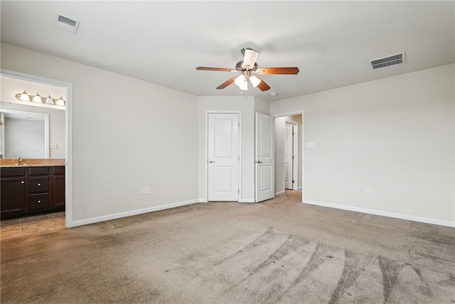 unfurnished bedroom featuring baseboards, light carpet, ensuite bathroom, and ceiling fan