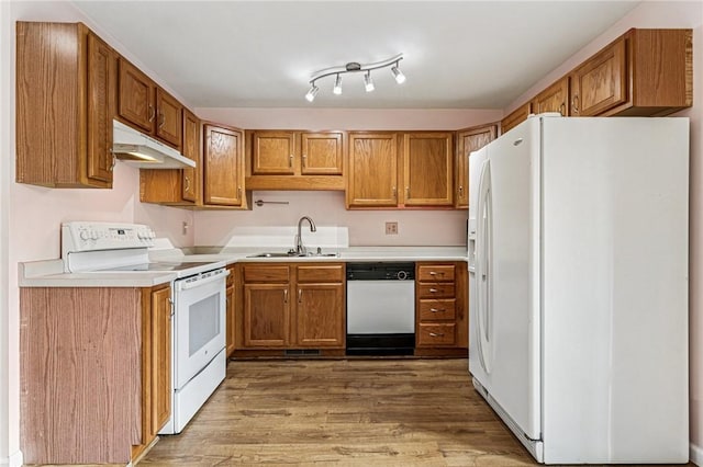kitchen with white appliances, under cabinet range hood, a sink, light wood finished floors, and brown cabinets
