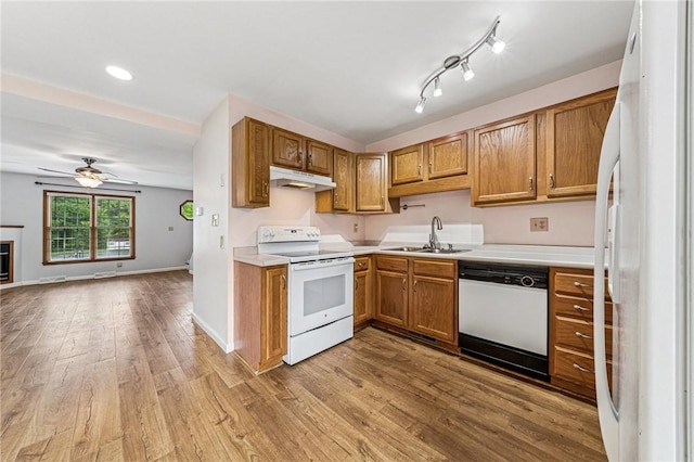 kitchen with white appliances, a sink, under cabinet range hood, open floor plan, and light countertops