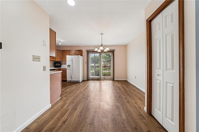 kitchen featuring white refrigerator with ice dispenser, a chandelier, dark wood finished floors, brown cabinetry, and light countertops