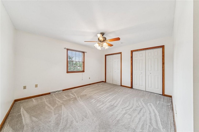 unfurnished bedroom featuring two closets, carpet floors, and baseboards