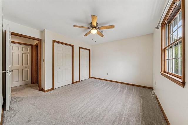 unfurnished bedroom with two closets, carpet flooring, baseboards, and a ceiling fan