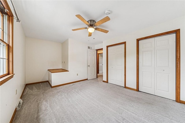 unfurnished bedroom with two closets, carpet flooring, baseboards, and a ceiling fan