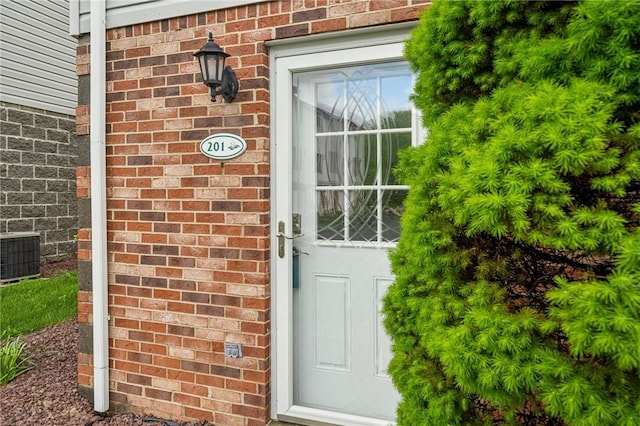 view of exterior entry with brick siding and central AC unit