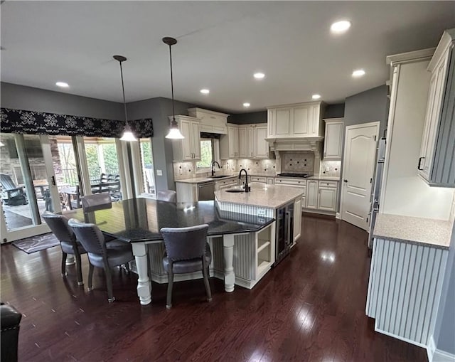 kitchen with a center island with sink, stainless steel dishwasher, a sink, dark wood-style flooring, and cooktop