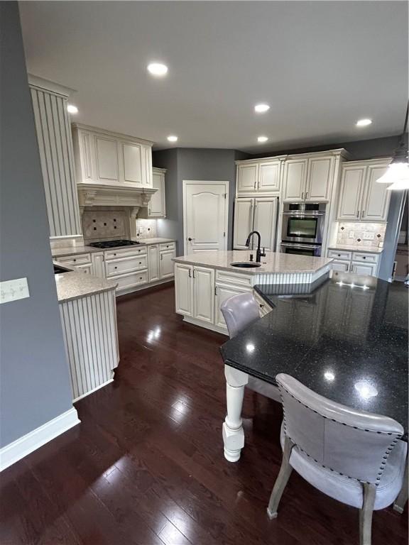 kitchen with premium range hood, black stovetop, backsplash, a sink, and recessed lighting