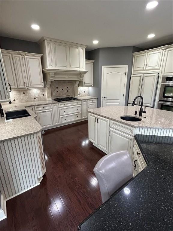 kitchen featuring a sink, black gas stovetop, stainless steel double oven, backsplash, and light stone counters