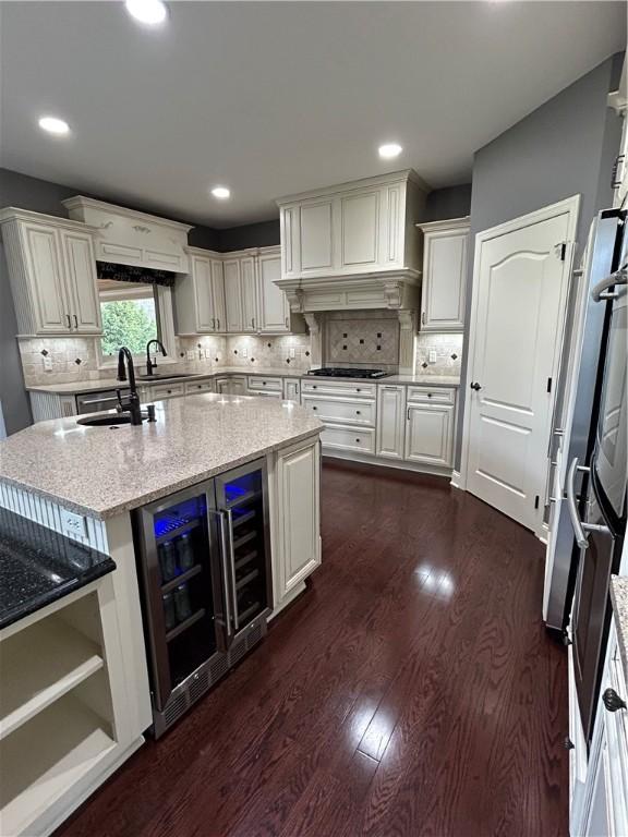 kitchen with a sink, dark wood-type flooring, beverage cooler, light stone countertops, and decorative backsplash